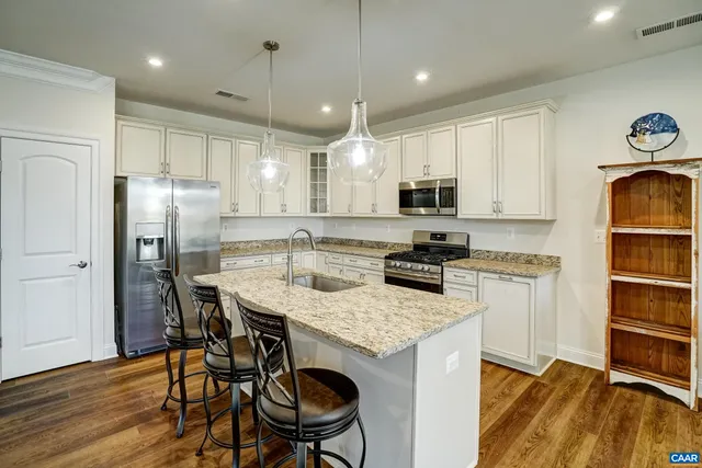 a kitchen with stainless steel appliances granite countertop a stove a refrigerator a microwave a sink and a dining table with wooden floor