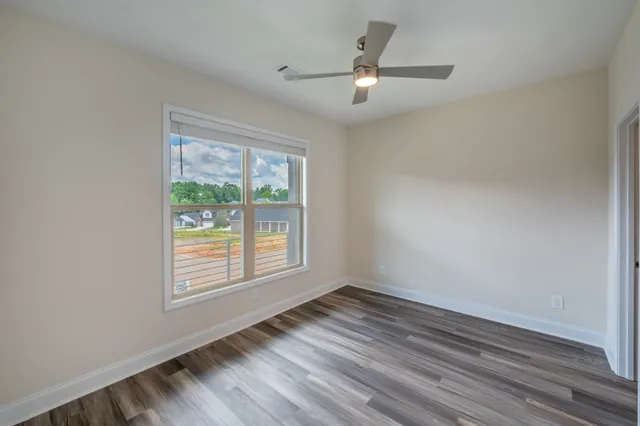 an empty room with wooden floor fan and windows