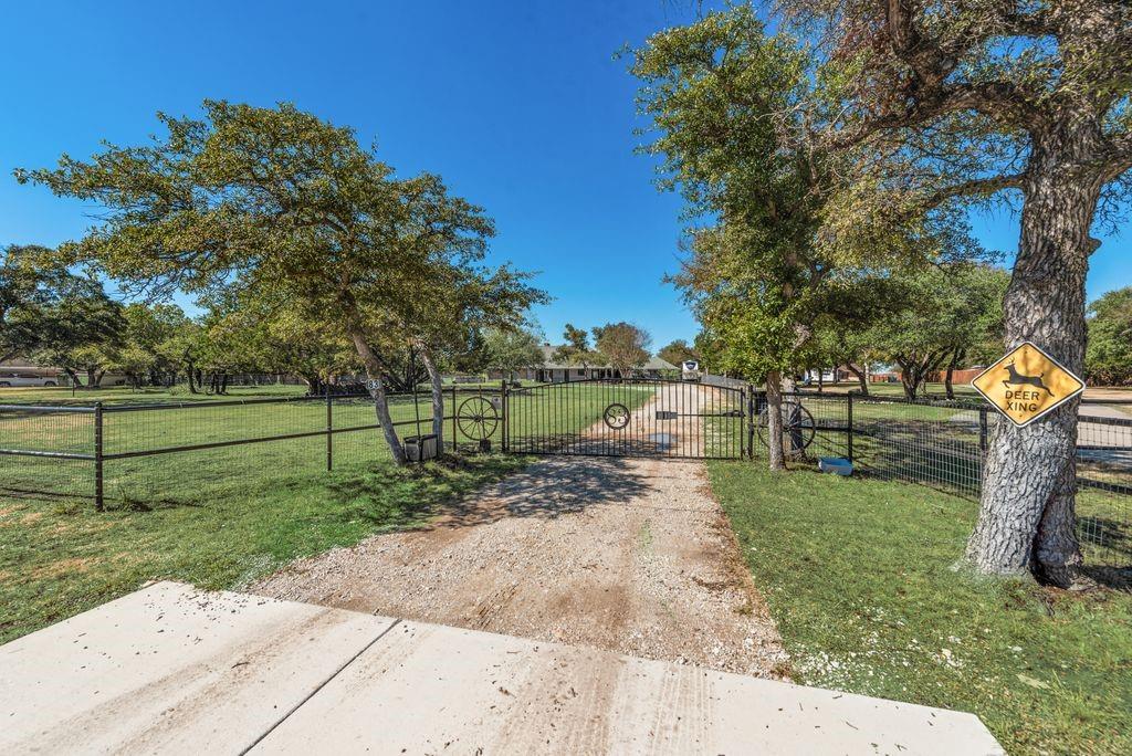 83 Crown Road Willow Park, TX 76087 - Photo 25 of 35 Gated entry with a gravel driveway, surrounded by mature trees, and a wire mesh fence