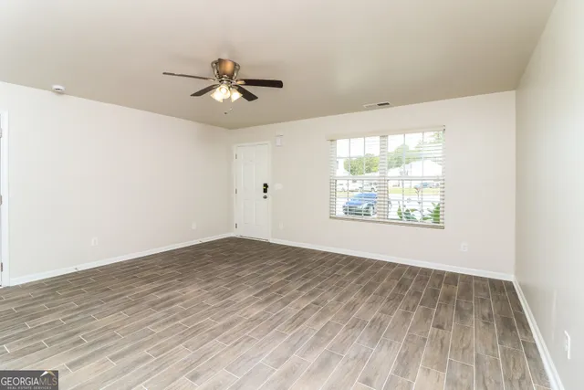 an empty room with wooden floor ceiling fan and windows