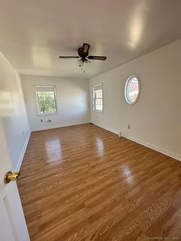 an empty room with wooden floor window and ceiling fan