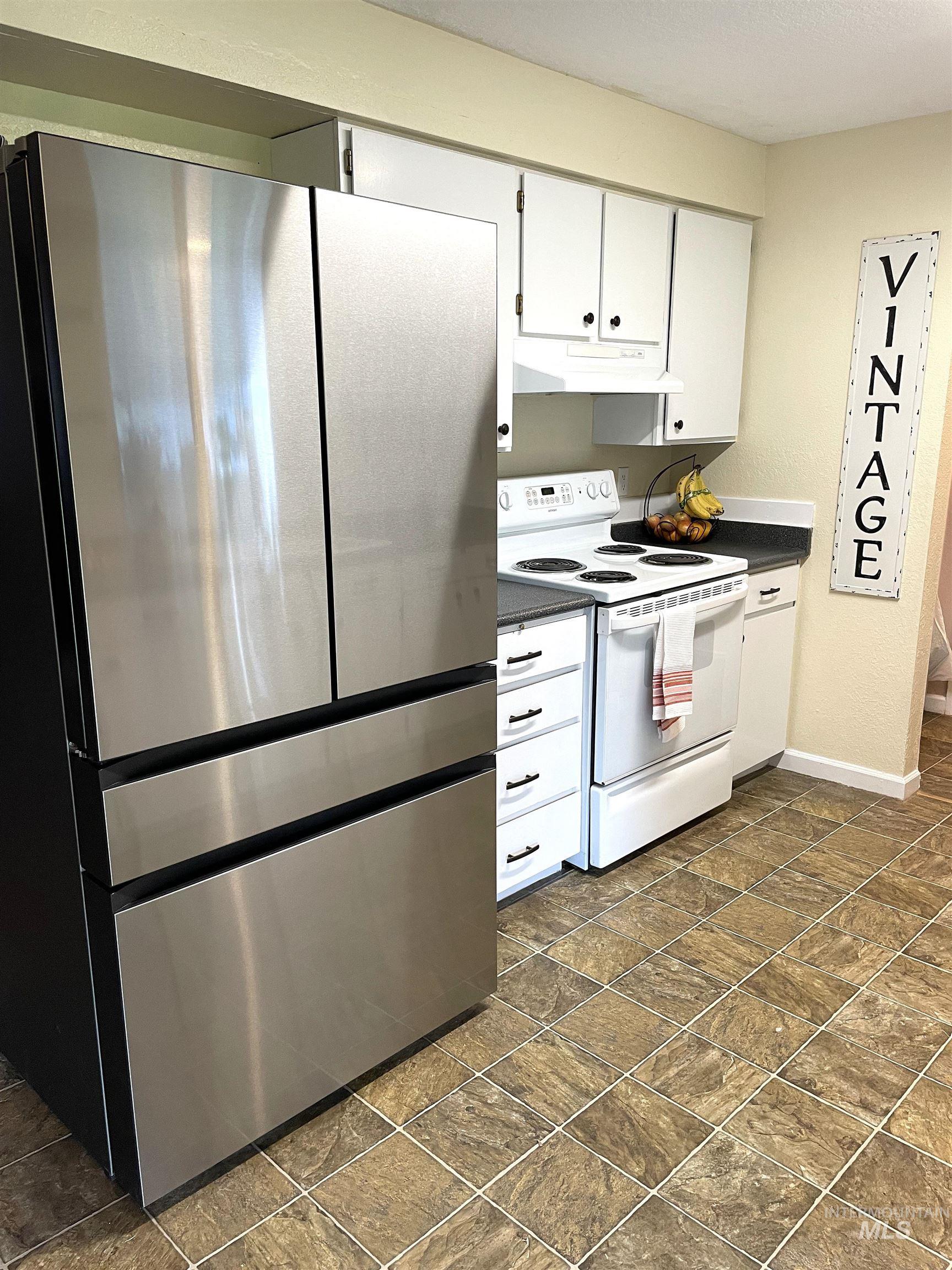 12733 South Five Mile Road Kuna, ID 83634 - Photo 7 of 21 Kitchen with freestanding refrigerator, electric range, white cabinetry, dark countertops, and under cabinet range hood