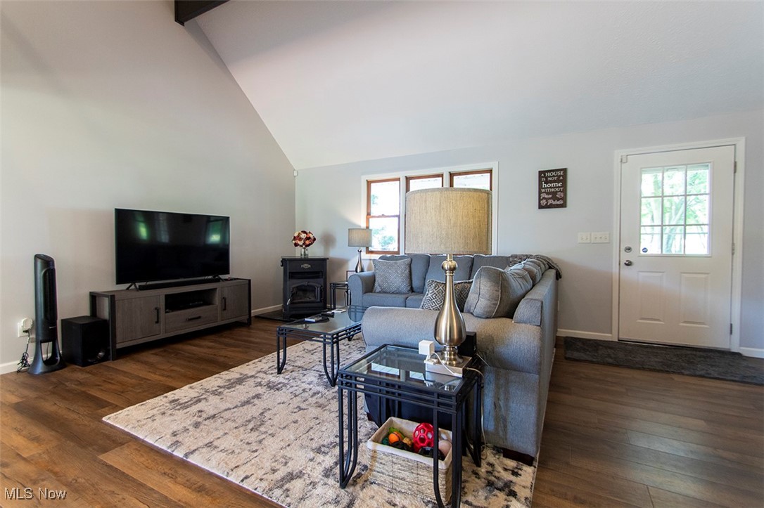 Living area featuring plenty of natural light, wood finished floors, a wood stove, and high vaulted ceiling