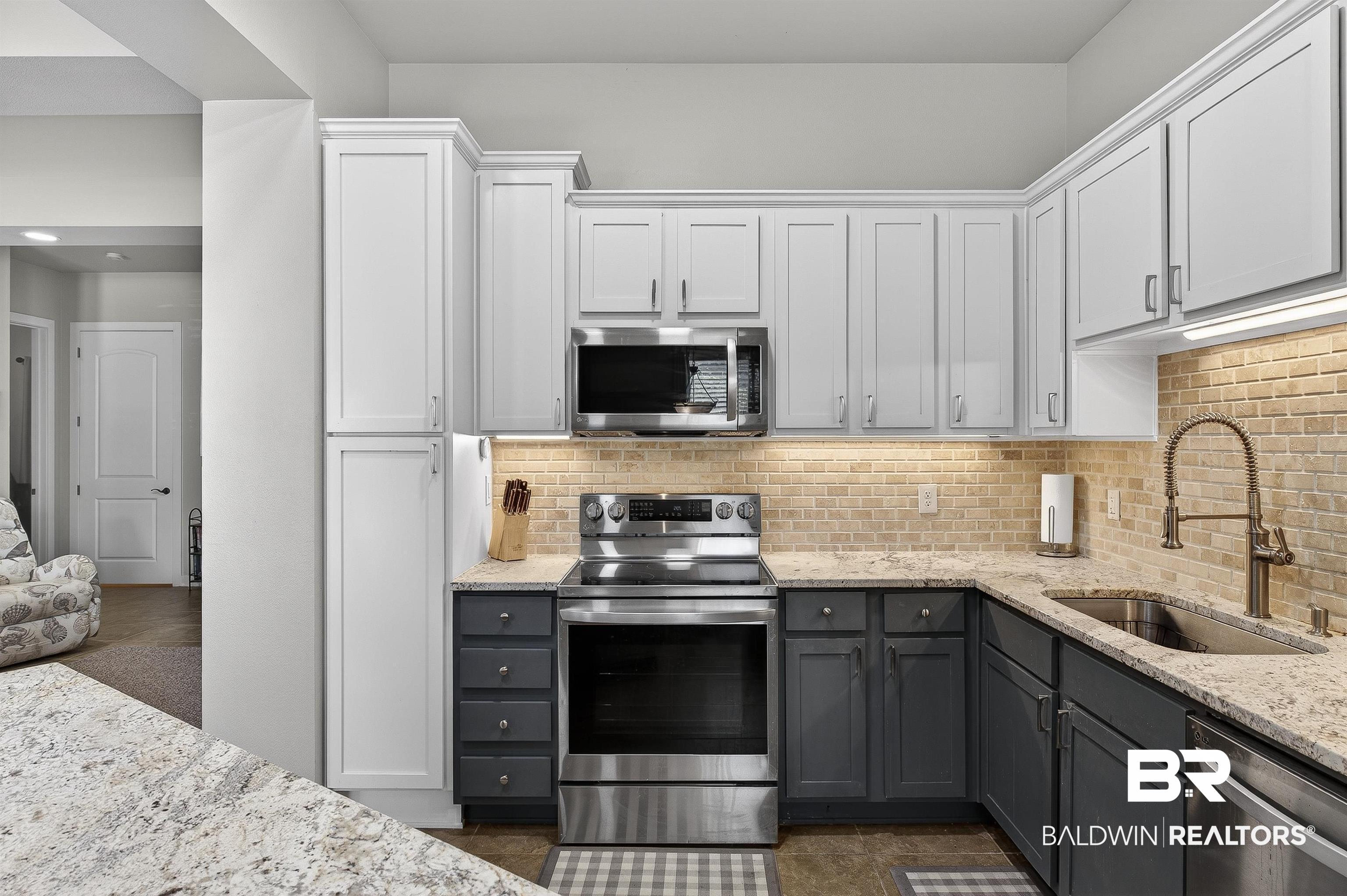 1430 West Regency Road, Unit I102 Gulf Shores, AL 36542 - Photo 10 of 31 Kitchen with stainless steel appliances, two tone cabinetry, light stone countertops, and backsplash