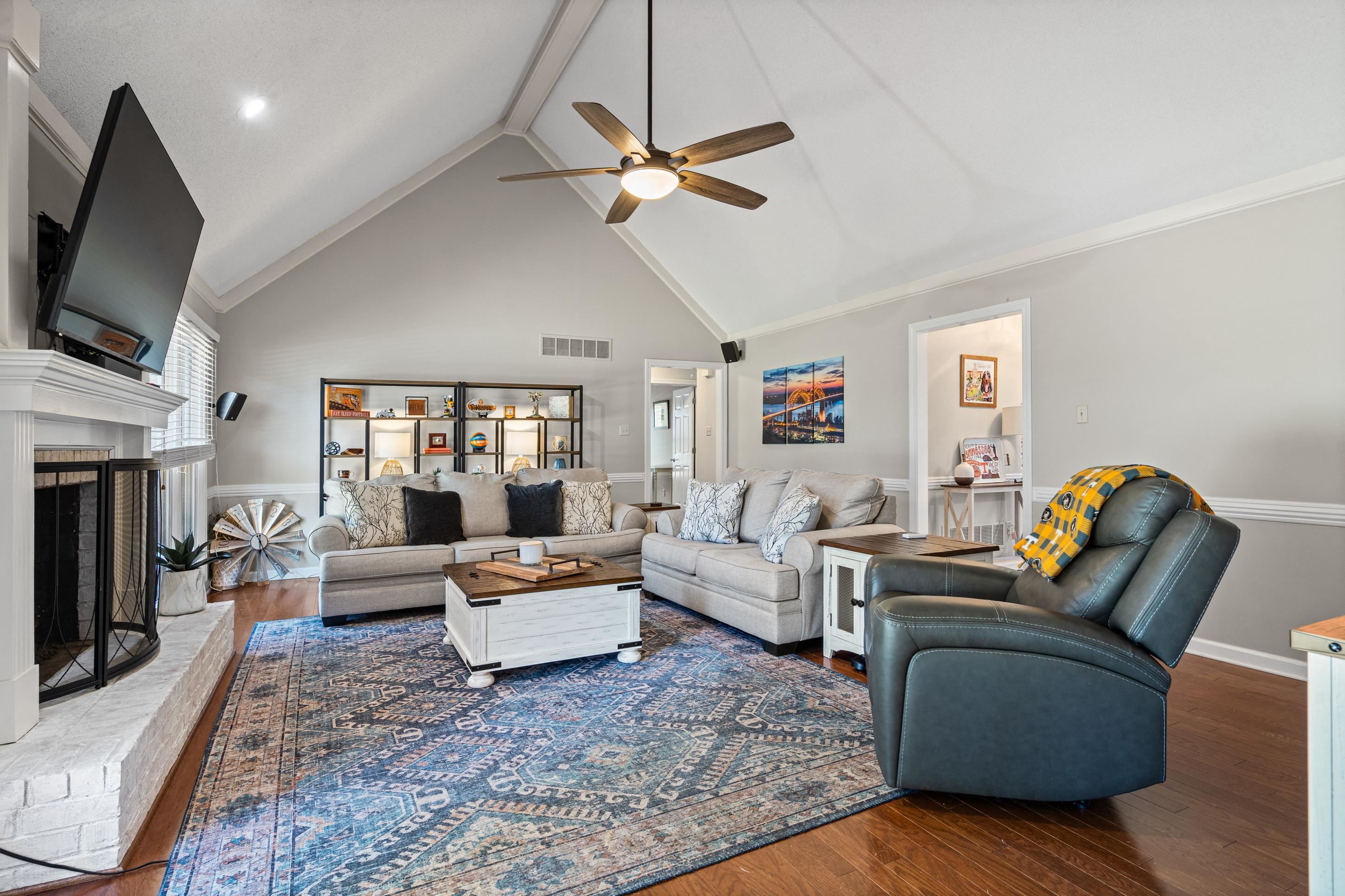 304 Spring Mill Road Collierville, TN 38017 - Photo 11 of 32 Living room featuring a vaulted ceiling with a ceiling fan, a painted brick fireplace with a white mantel, wood-finish flooring, and built-in shelving with integrated lighting