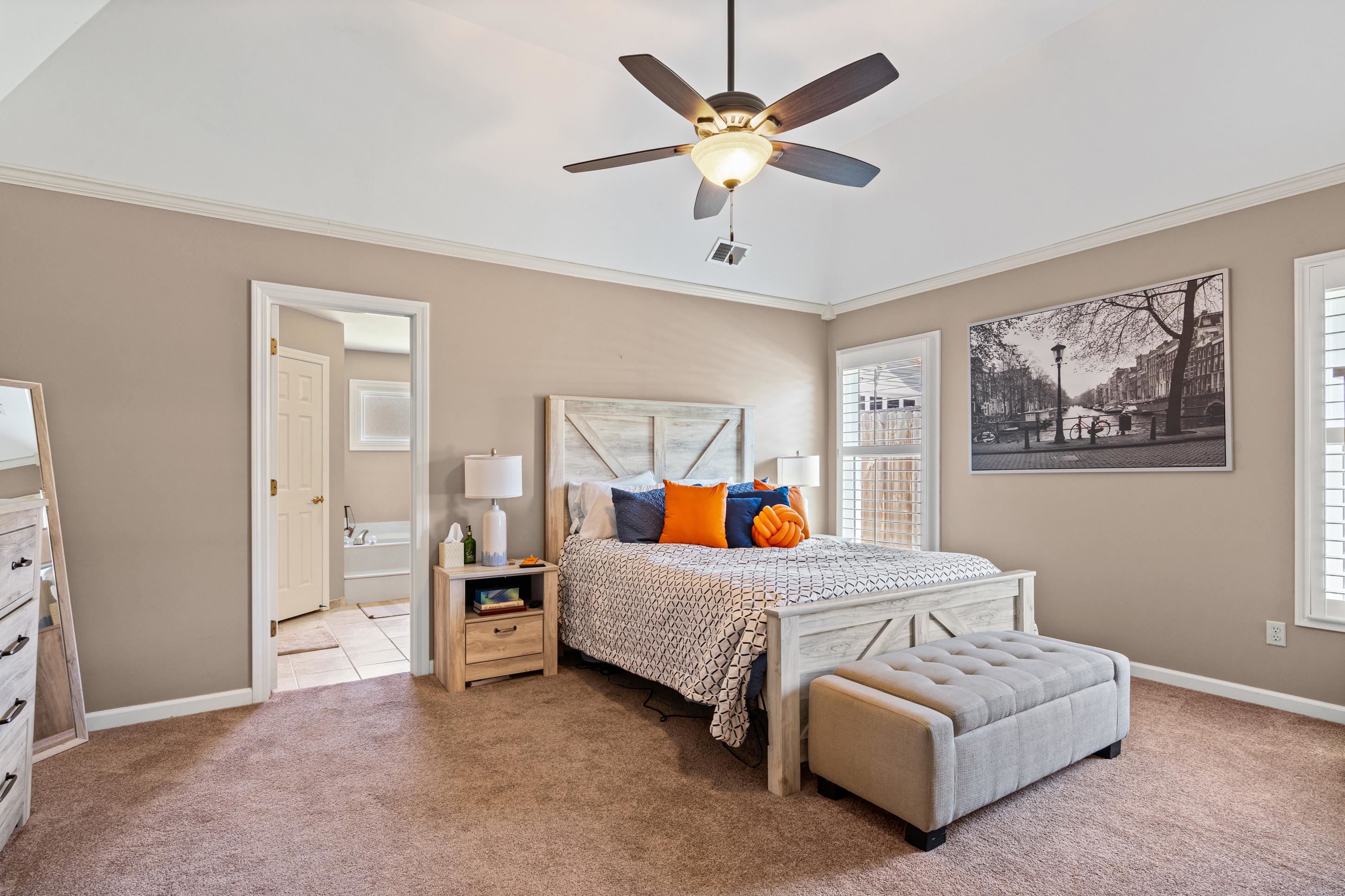 304 Spring Mill Road Collierville, TN 38017 - Photo 14 of 32 Carpeted bedroom featuring a vaulted ceiling with a fan light fixture, two windows with plantation shutters, crown molding, and an open doorway to a tiled bathroom with a built-in tub