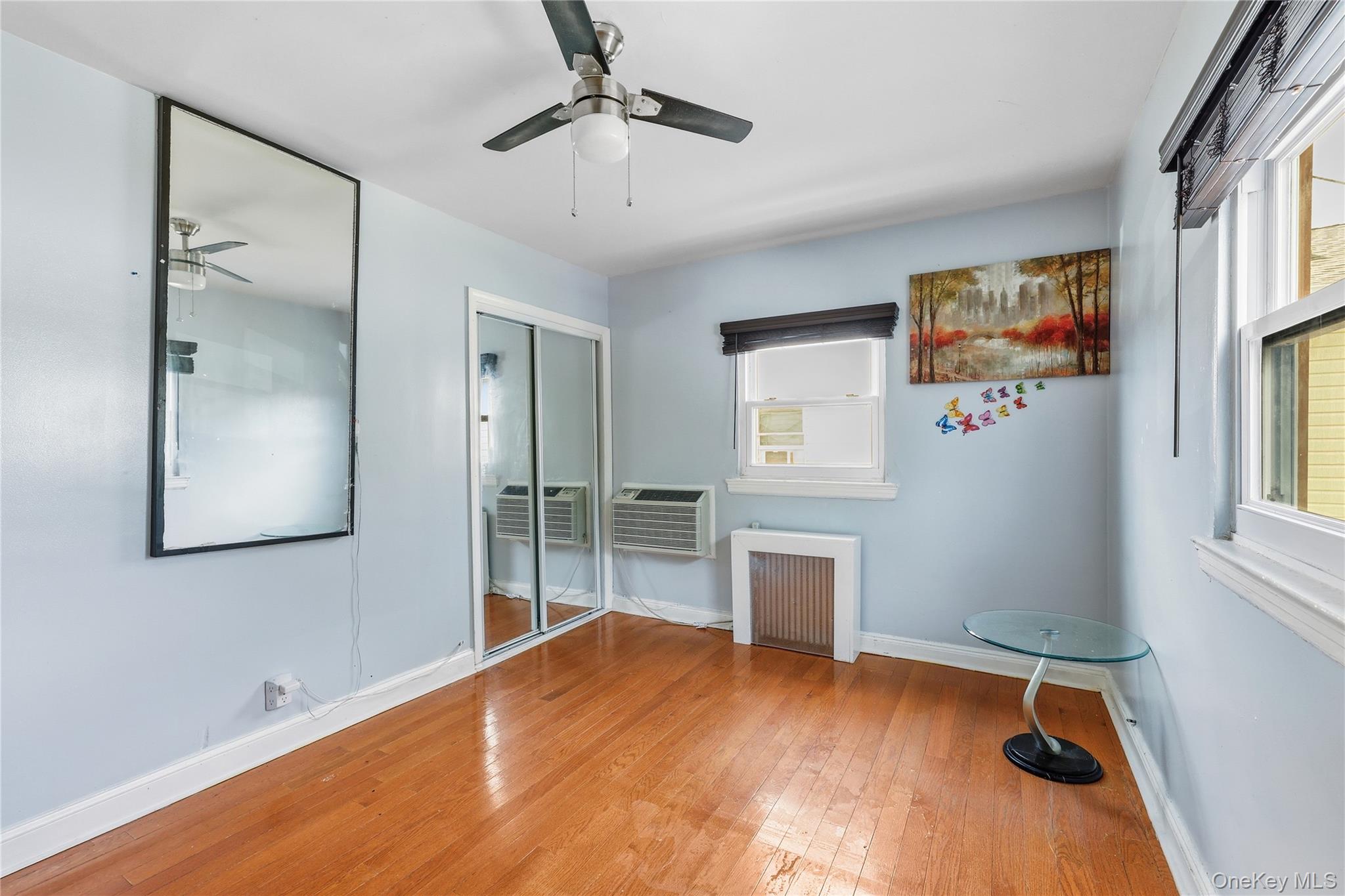 83-39 252nd Street Queens, NY 11426 - Photo 17 of 26 Room featuring wood-finish flooring, a ceiling fan, sliding mirror closet doors, and multiple windows with blinds
