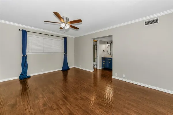 a view of an empty room with wooden floor and a ceiling fan