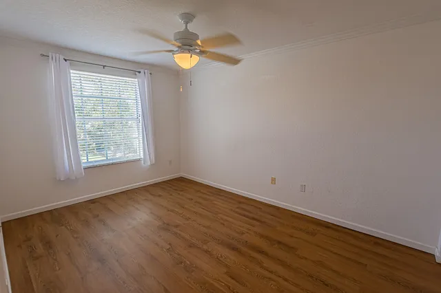 an empty room with wooden floor fan and windows