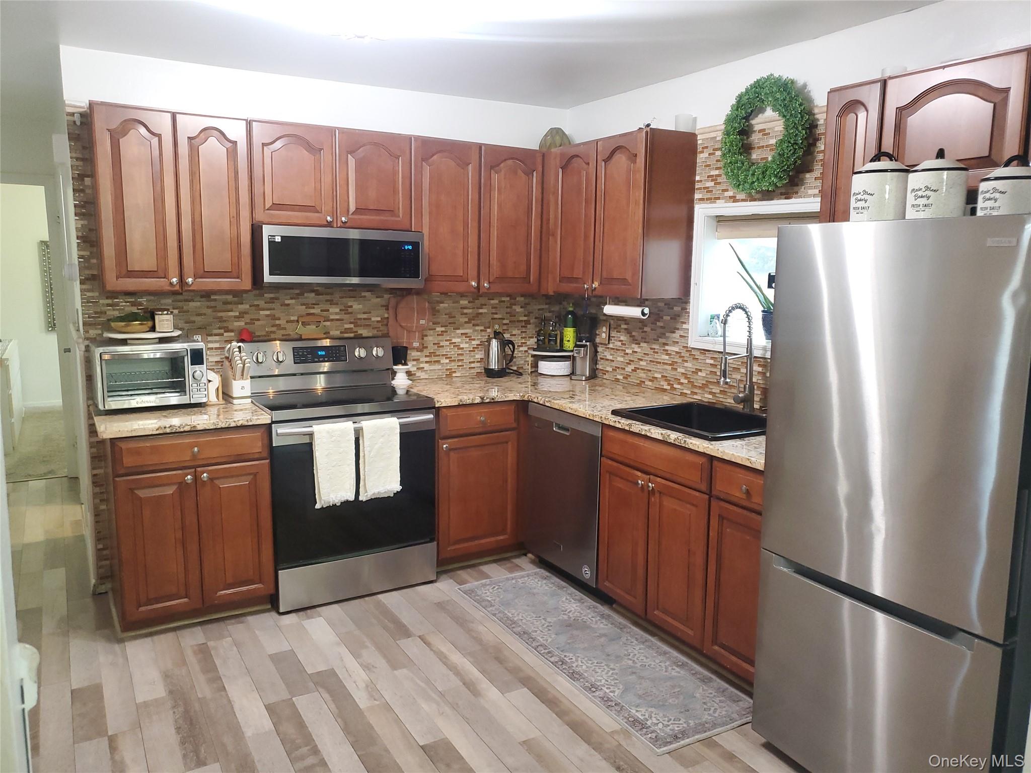 117 North Coleman Road Centereach, NY 11720 - Photo 6 of 26 Kitchen with appliances with stainless steel finishes, light stone countertops, light wood-type flooring, and tasteful backsplash