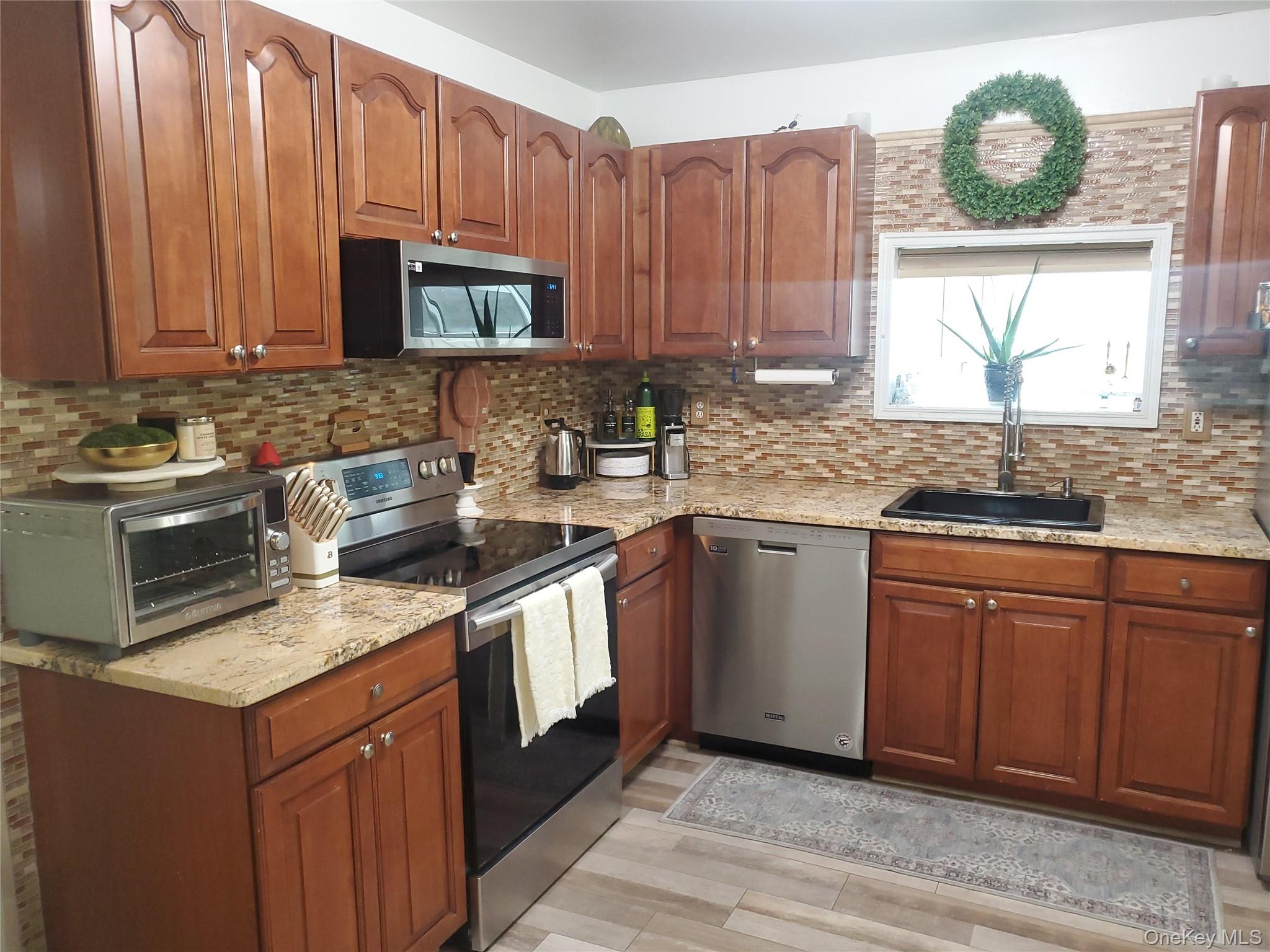 117 North Coleman Road Centereach, NY 11720 - Photo 8 of 26 Kitchen with stainless steel appliances, light stone countertops, brown cabinets, and light wood-style flooring