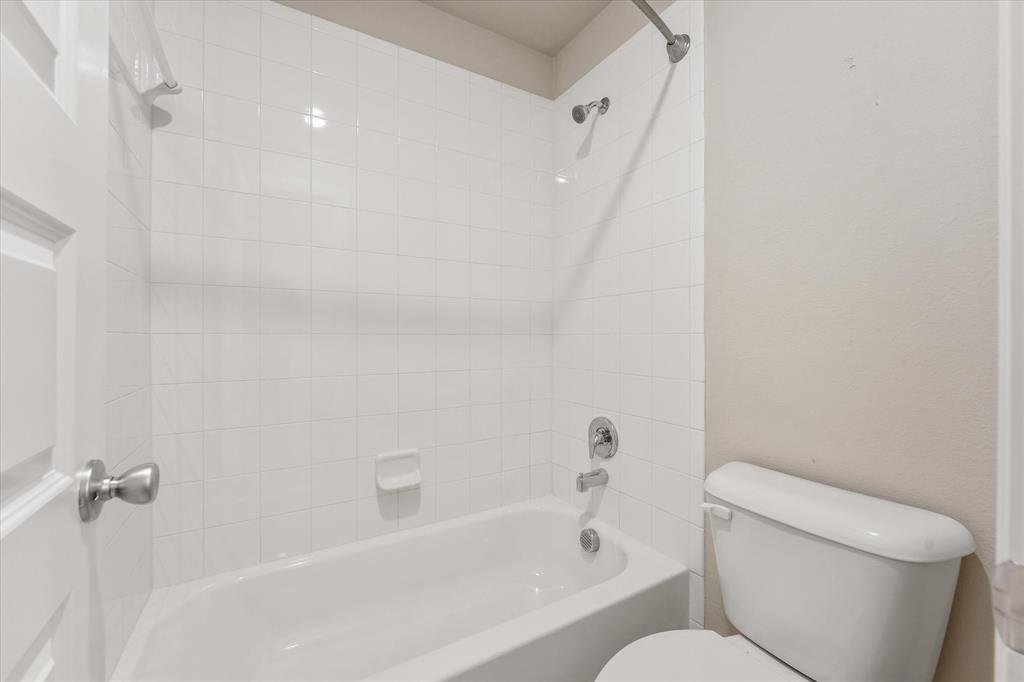 2044 Longbridge Road Forney, TX 75126 - Photo 27 of 40 Bathtub with white tile surround, chrome fixtures, and a white toilet