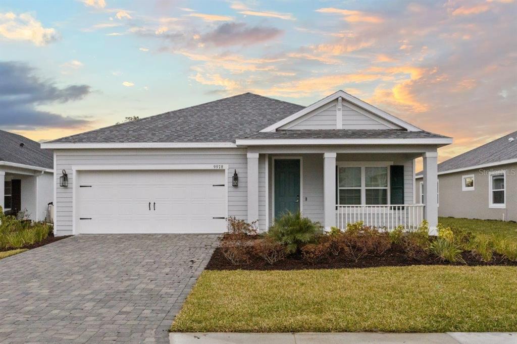 Front elevation featuring a large covered front porch, paver driveway, and fresh landscaping.