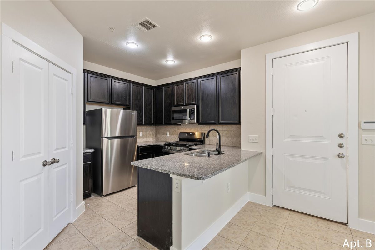 2225 Katy Lane, Unit B Georgetown, TX 78626 - Photo 8 of 22 Kitchen with stainless steel appliances, light stone countertops, a peninsula, and light tile patterned floors