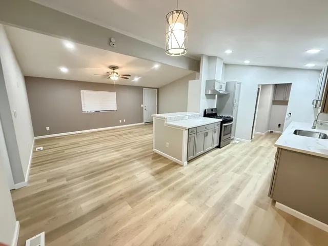 a large room with kitchen island a refrigerator a sink dishwasher a stove and a dining table with wooden floor