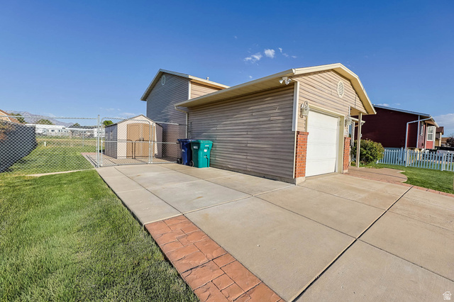5896 South 3950th Street West Roy, UT 84067 - Photo 23 of 29 View of home's exterior featuring brick siding, driveway, an outbuilding, and an attached garage