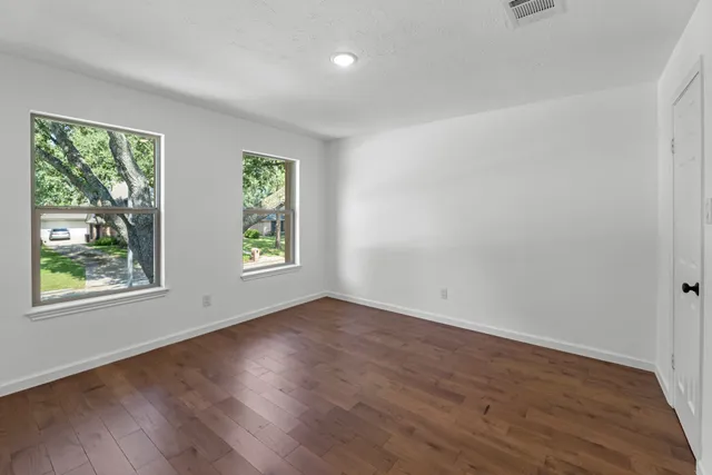 a view of an empty room with wooden floor and windows