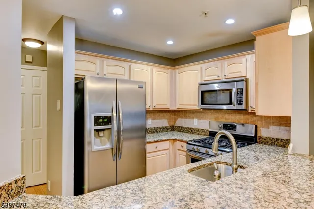 a kitchen with stainless steel appliances granite countertop a refrigerator a stove and a sink with wooden floor