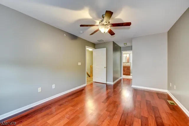 a view of an empty room with wooden floor and a ceiling fan