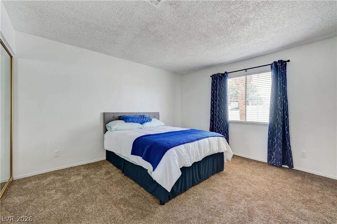 1751 East Reno Avenue, Unit 228 Las Vegas, NV 89119 - Photo 26 of 39 Comfortable bedroom with plush carpet and a sun-filled window dressed with blinds and drapes.