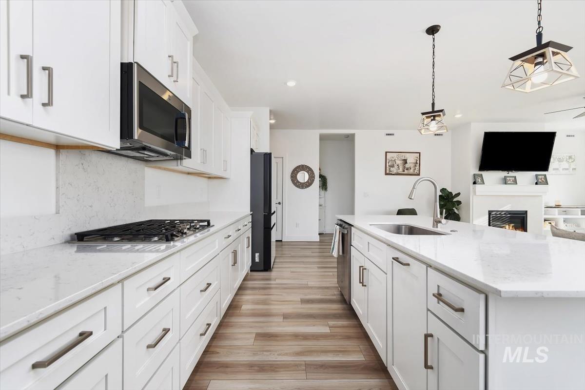 14361 Fractus Drive Caldwell, ID 83607 - Photo 10 of 50 Kitchen featuring white cabinetry, light stone countertops, decorative light fixtures, a glass covered fireplace, and an island with sink
