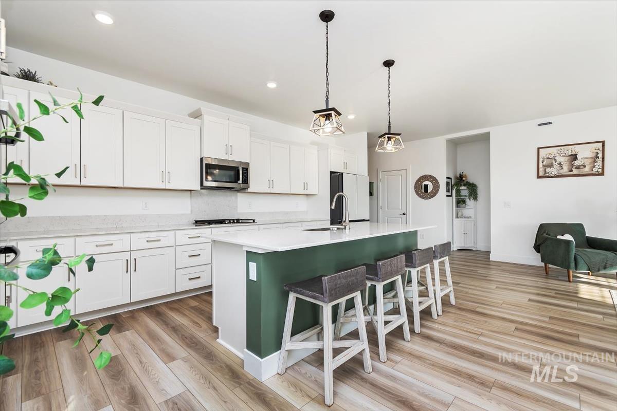 14361 Fractus Drive Caldwell, ID 83607 - Photo 9 of 50 Kitchen with white cabinets, a breakfast bar area, a center island with sink, hanging light fixtures, and stainless steel microwave