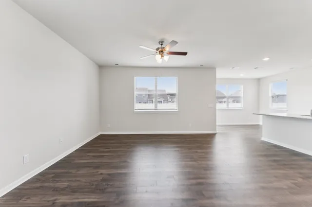 an empty room with wooden floor chandelier fan and windows