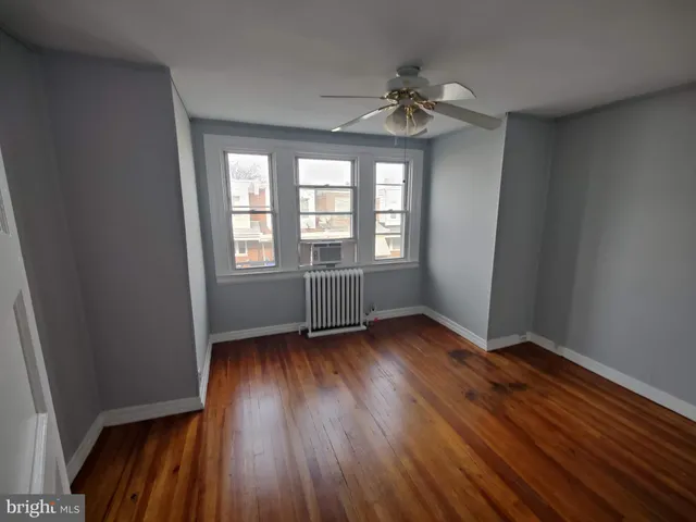 an empty room with wooden floor fan and window