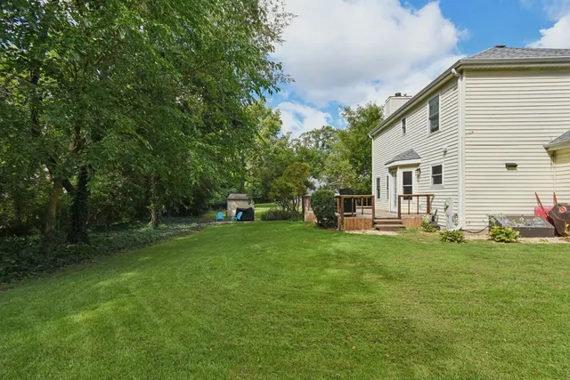 a view of a white house in front of a big yard with plants and large trees