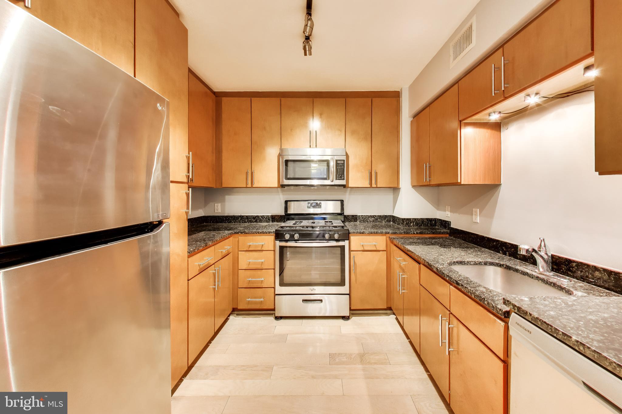 915 E Street Northwest, Unit 414 Washington, DC 20004 - Photo 11 of 35 a kitchen with granite countertop a refrigerator a sink and white cabinets
