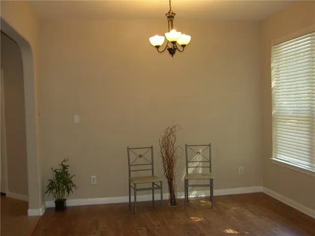 an empty room with wooden floor chandelier and windows