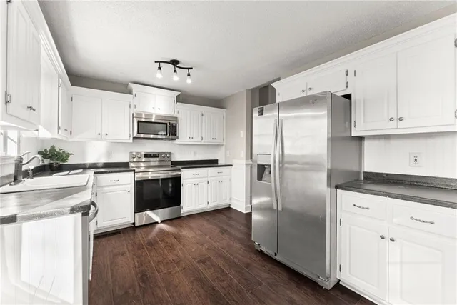 a kitchen with kitchen island granite countertop a refrigerator a sink and white cabinets with wooden floor