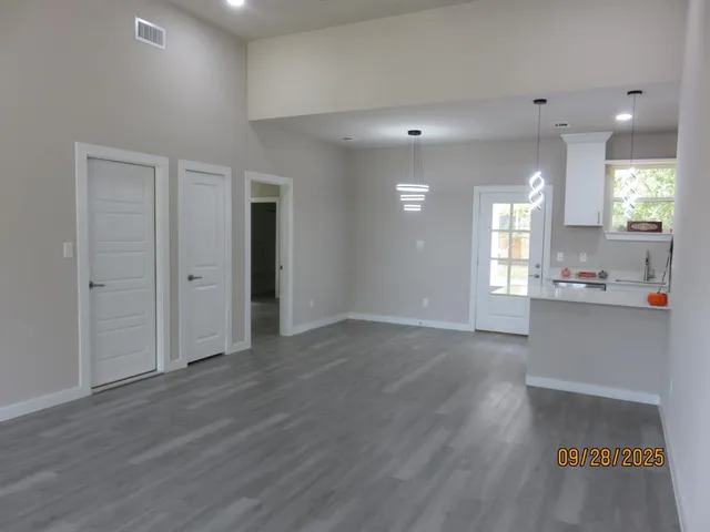 a view of an empty room and kitchen with wooden floor