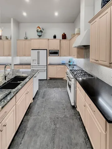 a large white kitchen with stainless steel appliances granite countertop a stove a sink a refrigerator and white cabinets