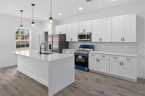 a kitchen with stainless steel appliances white cabinets a sink a stove a refrigerator and microwave