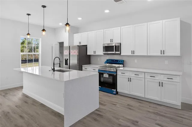 a kitchen with stainless steel appliances white cabinets a sink a stove a refrigerator and microwave