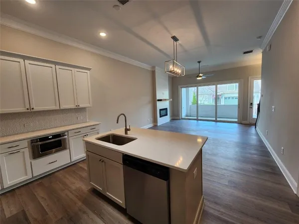 a kitchen that has a sink a microwave oven a stove and white cabinets with wooden floor
