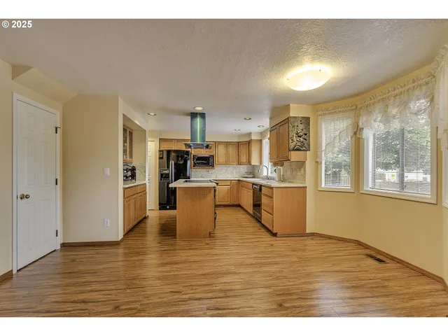 a living room with stainless steel appliances kitchen island granite countertop a refrigerator a sink a stove and a wooden cabinets