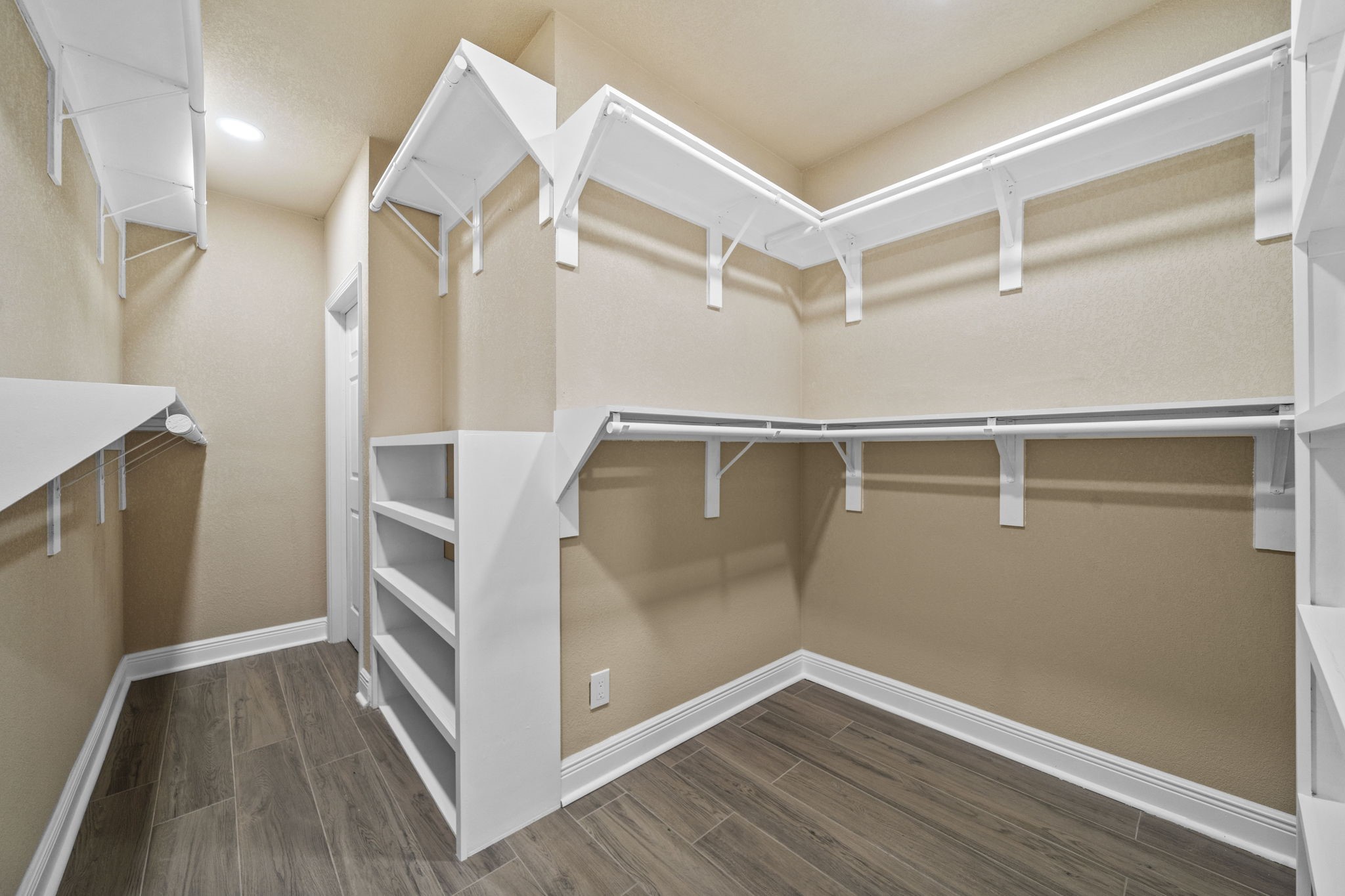 14215 Spindle Arbor Road Cypress, TX 77429 - Photo 23 of 47 This photo shows a spacious walk-in closet with ample shelving and hanging space. The neutral walls and wood-look flooring create a warm, inviting atmosphere, while built-in shelves offer convenient storage solutions.