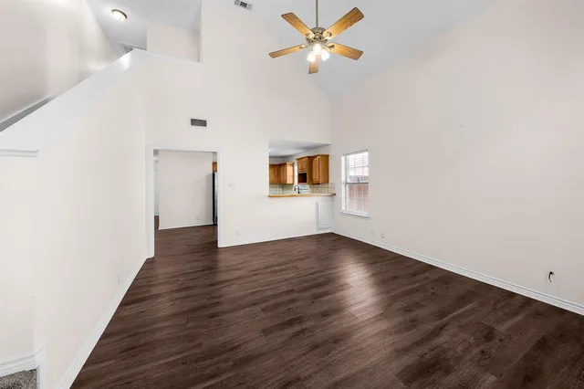 a view of an empty room with wooden floor and a ceiling fan