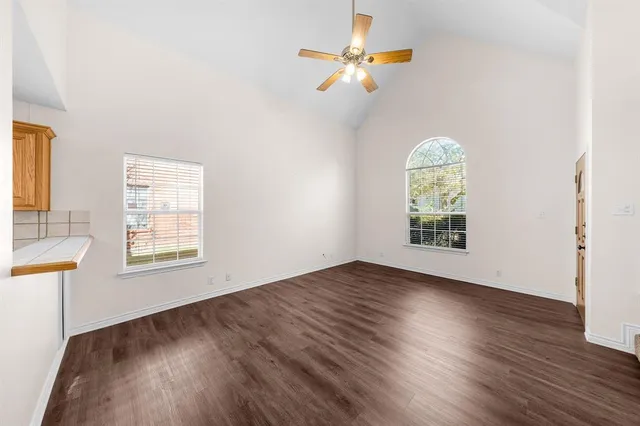 an empty room with wooden floor a ceiling fan and windows