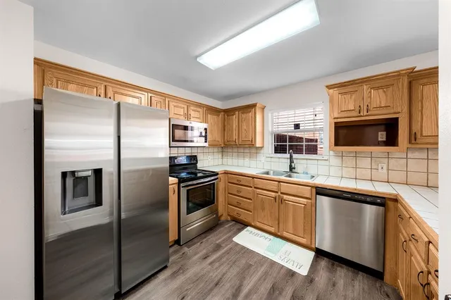 a kitchen with stainless steel appliances granite countertop a refrigerator a sink a stove top oven and a refrigerator with wooden floor