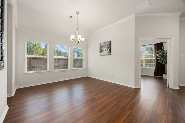 an empty room with wooden floor chandelier and windows