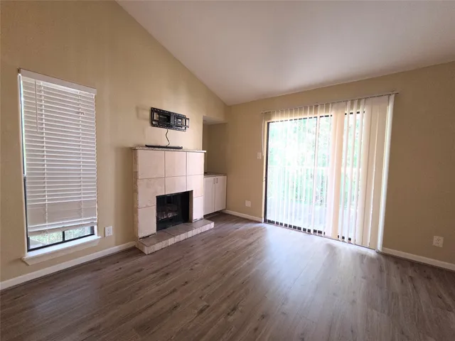 an empty room with wooden floor fireplace and windows