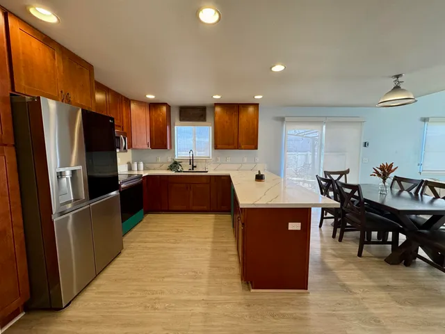 a large kitchen with stainless steel appliances granite countertop a refrigerator a sink dishwasher a dining table and chairs with wooden floor