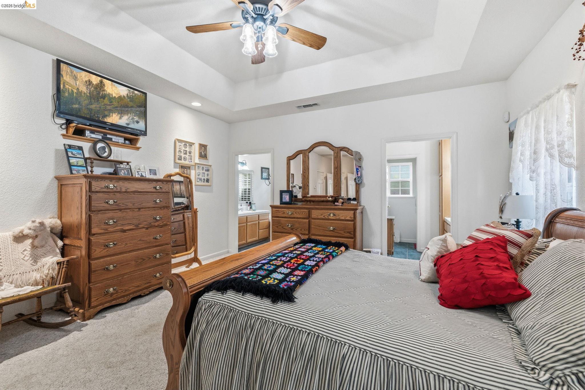 18450 Lambert Lake Road Sonora, CA 95370 - Photo 23 of 87 Spacious bedroom featuring a tray ceiling, ceiling fan, carpet flooring, and a doorway leading to a bathroom