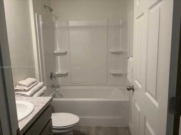 a bathroom with a granite countertop bathtub shower sink vanity and toilet