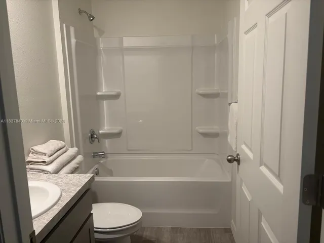 a bathroom with a granite countertop bathtub shower sink vanity and toilet