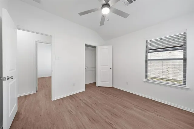 an empty room with wooden floor chandelier fan and windows