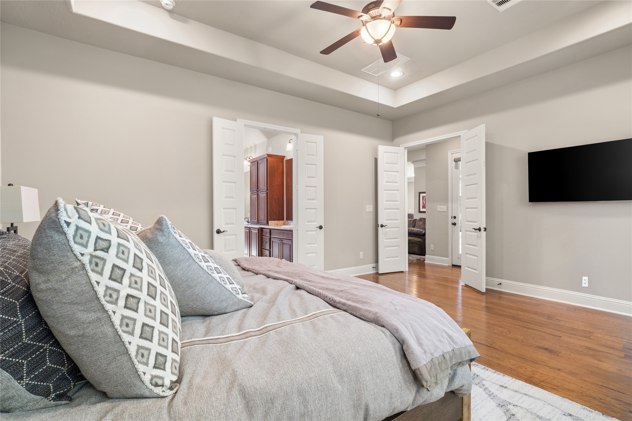 19813 Cullen Ridge Drive Porter, TX 77365 - Photo 22 of 44 Experience ultimate relaxation in this inviting primary bedroom, featuring elegant tray ceilings, warm wood flooring, and a seamless flow into a luxurious ensuite, promising serene and sophisticated living.